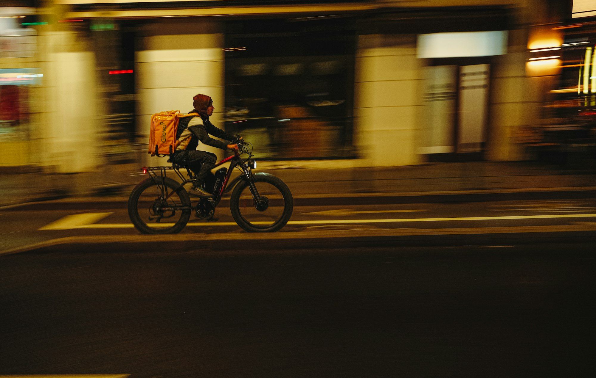 Fahrradkurier mit Lieferrucksack fährt nachts durch die Stadt