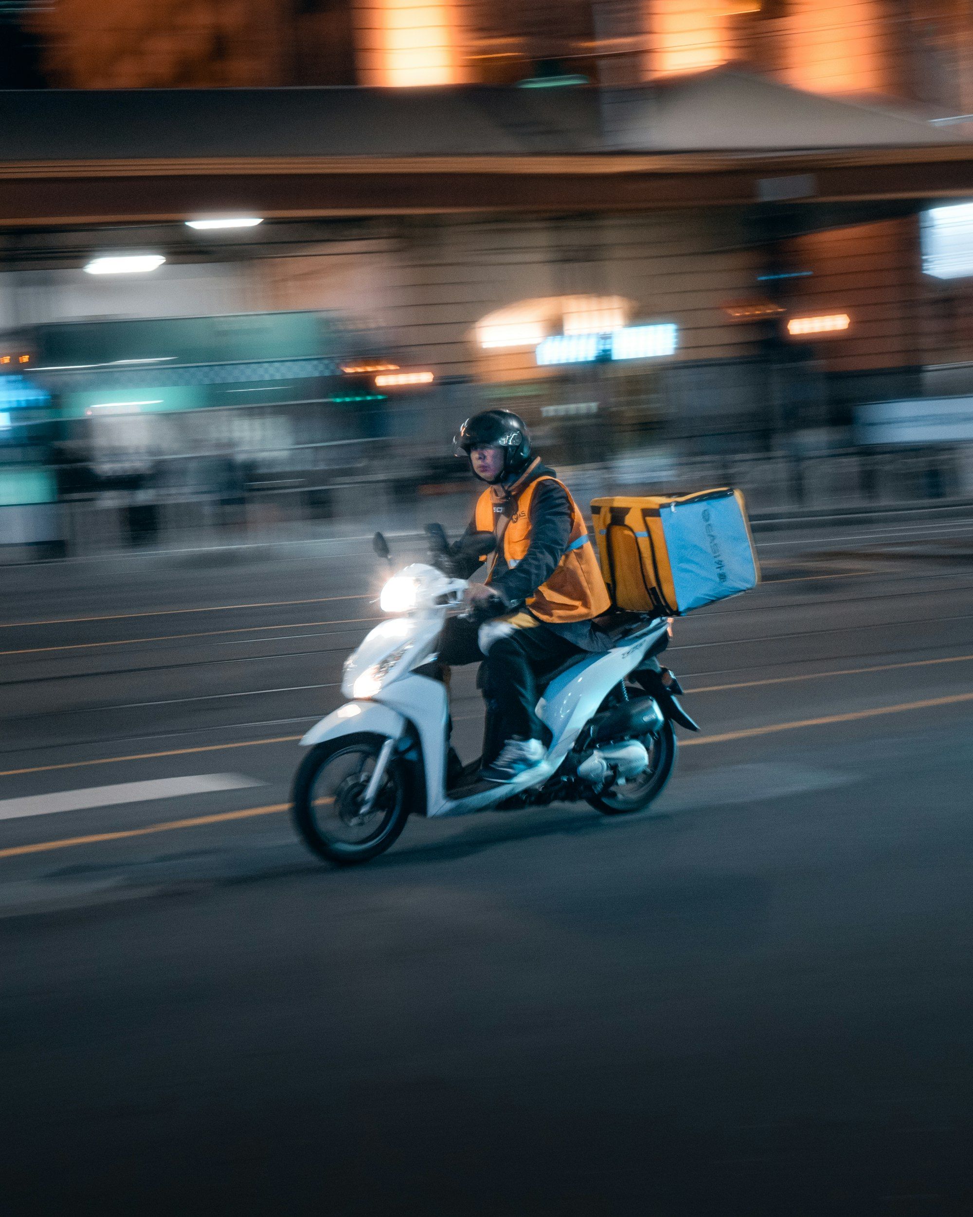 Lieferfahrer mit Thermobox auf einem Motorroller bei Nacht