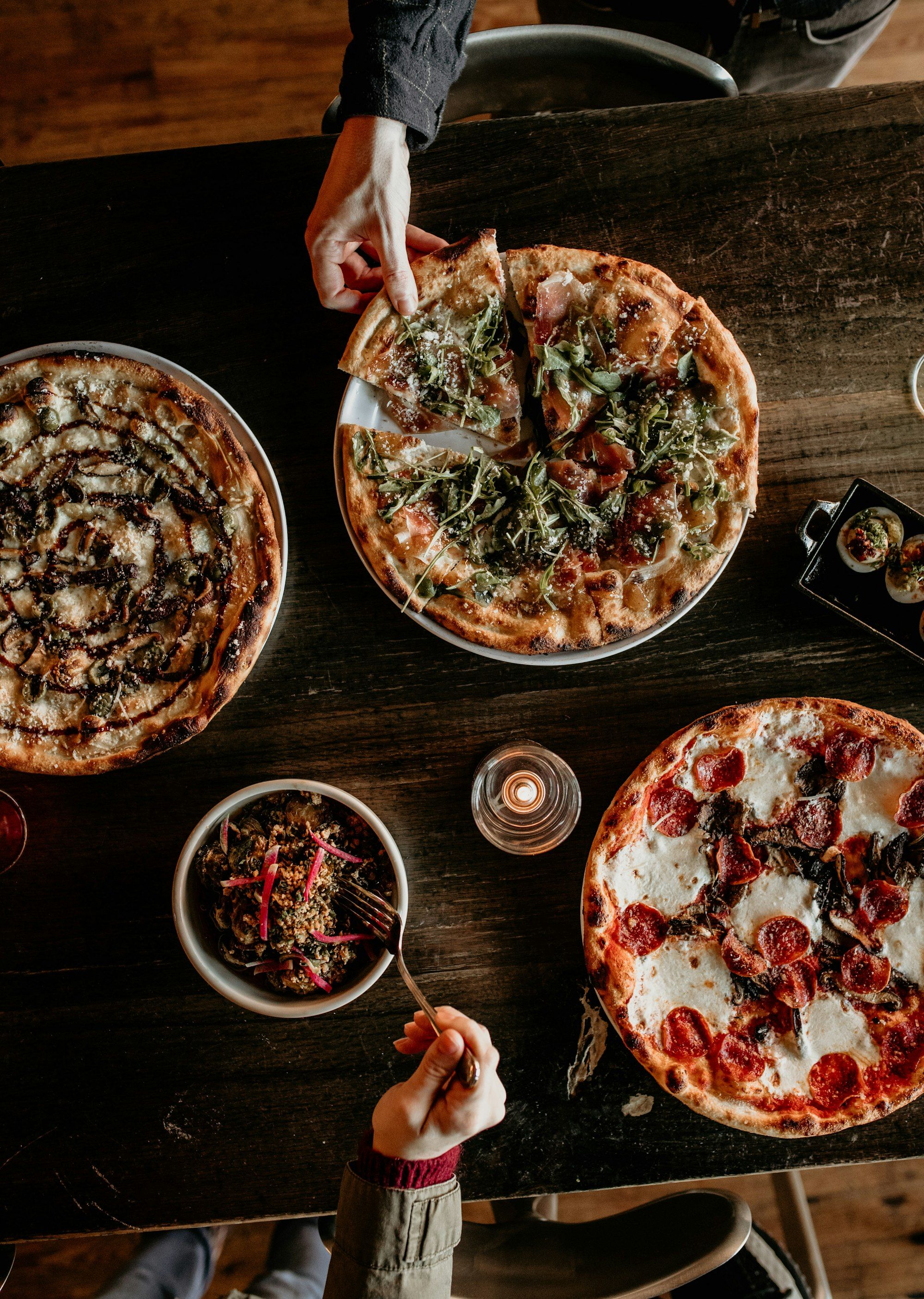 Mehrere Pizzen und Beilagen von oben auf einem dunklen Holztisch